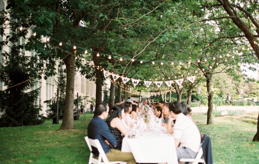 Guests gathered at a longtable in David Thompson School Farm sharing good food and drink under bunting which spells out 'Community'